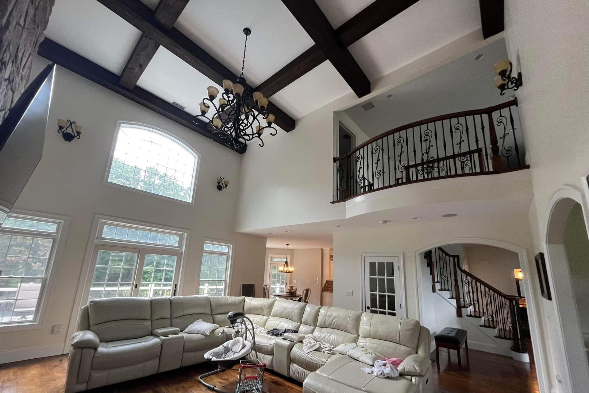 Spacious living room with a vaulted ceiling, dark beams, and ornate staircase railings